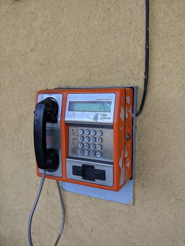 red and black telephone mounted on beige wall